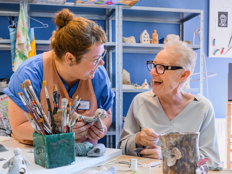 Eine Kunsttherapeutin und eine Patientin lachen gemeinsam